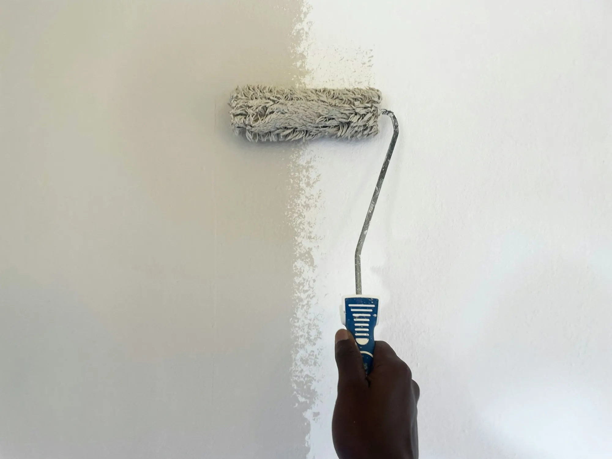 Paint roller applying a fresh coat of white paint to an interior wall